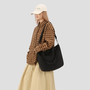 Side view of a black canvas tote bag with adjustable strap worn by a female model