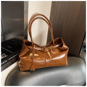 Detailed close-up of brown glossy leather tote bag with gold hardware on a gray sofa