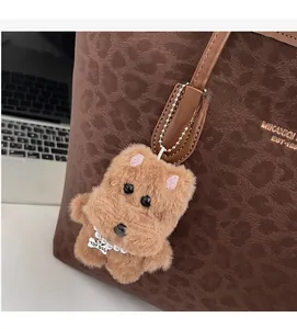 Close-up of a light brown plush dog charm with pearl necklace and metal tag on a bag