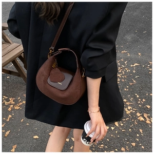 Detail of dark brown crescent crossbody bag with heart charm and matte finish