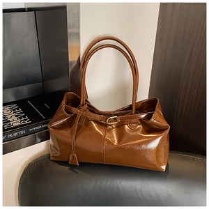 Detail of dark brown glossy leather tote bag with metal buckle and shoulder strap