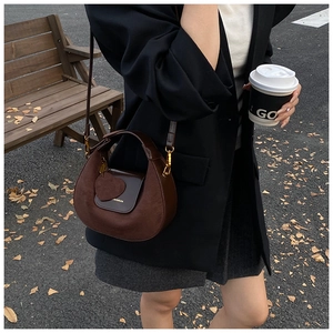 Dark brown matte crescent bag with gold hardware and heart charm shown on a model