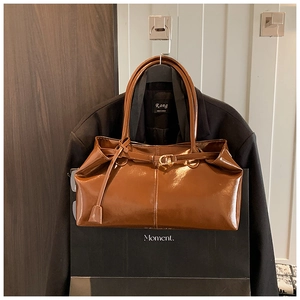 Detail of dark brown polished leather tote bag featuring a gold buckle and metal hardware