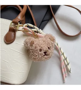 Detail of soft plush bear pendant with braided cord on a cream faux leather bucket bag