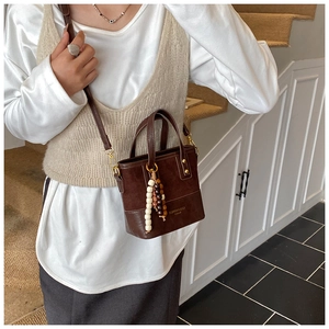 Sac seau bicolore marron avec breloque en perles porté par un mannequin en décor minimal