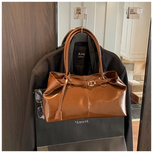 Detail of a brown glossy leather tote bag with slim handles on a black blazer