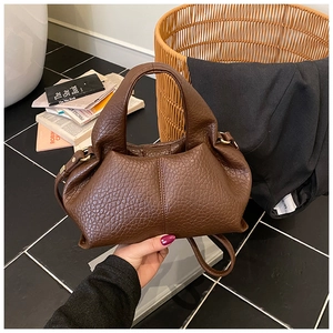 Detail of dark brown lychee leather handbag with golden hardware and adjustable strap