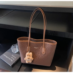 Detail of leopard print tote bag with plush bear charm and premium synthetic leather finish