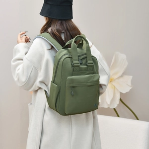 Rear view of a model wearing the olive green waterproof nylon backpack in a modern room