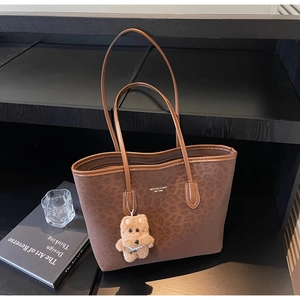 Close-up of leopard print tote bag with brown leather handles and plush bear charm