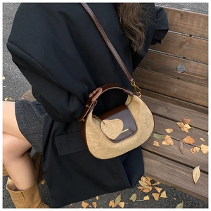 Detail of a brown leather semicircular bag with heart charm on a park bench