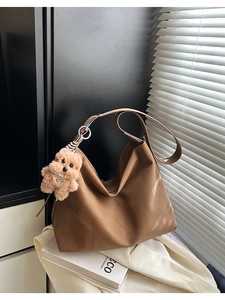 Dettaglio di una borsa tote in pelle marrone con texture morbida e ciondolo a orsetto