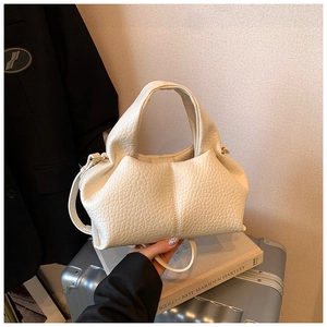 Detailed shot of white lychee texture cloud bag on art books with golden hardware