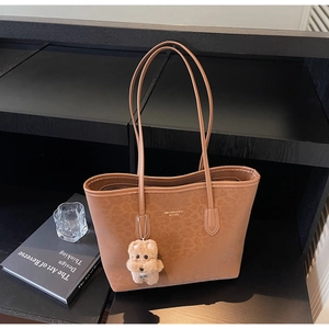 Close-up of brown tote bag featuring leopard pattern embossing and plush dog charm