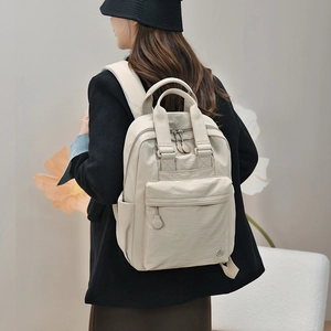 Close-up of a beige nylon backpack featuring multiple pockets and high-quality metal zippers