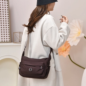 Detail of dark brown water-resistant nylon crossbody bag with multi-pocket design on model