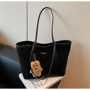 Detail of black leopard print tote bag with soft brown bear charm and white brand logo
