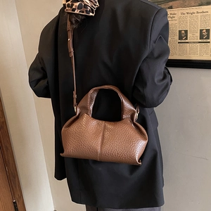 Detail view of brown pebbled leather texture on a soft pleated cloud crossbody bag