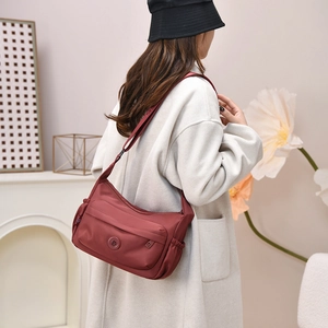 Deep red water-resistant nylon crossbody bag shown worn with a white coat and black hat