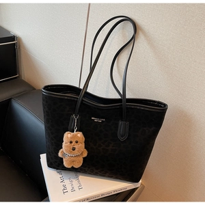 Detail of black leopard texture tote bag with plush bear charm on white design books
