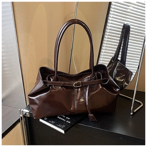 Detailed view of dark brown glossy patent leather tote bag with thin straps and buckle