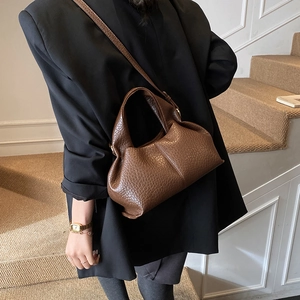 Detail of a dark brown pleated cloud bag with leather texture worn cross-body style