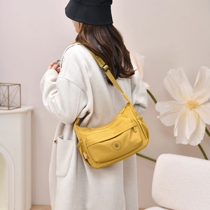 Detail view of mustard yellow nylon shoulder bag with adjustable strap and zip pockets
