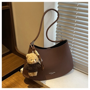 Detailed view of brown leather half-moon shoulder bag with cute teddy bear charm