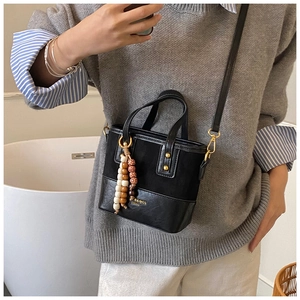 Détail du sac seau noir en cuir avec pendentifs en perles de bois et rivets métalliques