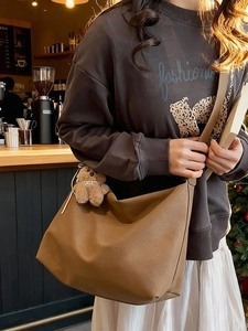 Borsa a tracolla a mezzaluna marrone scamosciata con ciondolo a orsetto in un accogliente caffè