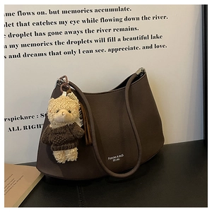 Detail of dark brown crescent shoulder bag featuring a cute plush bear charm and chic logo