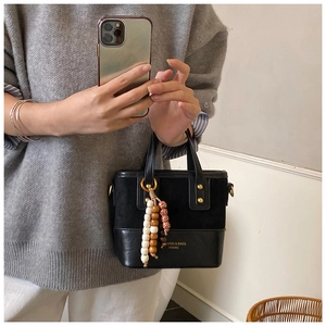 Detail of black crossbody bag featuring suede stitching and wooden bead tassel charms