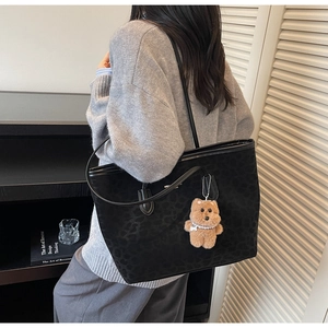 Detail of black leopard texture tote bag with a brown plush bear charm for a stylish look