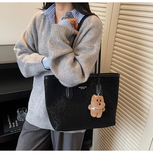 Detail of black leopard embossed tote bag with brand logo and brown plush bear charm