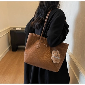 Detail of leopard print tote bag with plush bear charm and brand logo text on the front