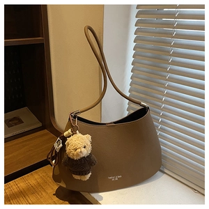 Detail of a brown hobo shoulder bag with cute teddy bear charm on a warm wooden background