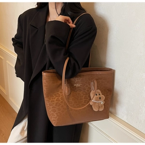 Detail of a brown leopard print tote bag featuring a cute plush dog charm and gold logo