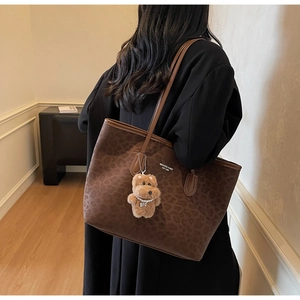 Detail of leopard print tote bag featuring a plush bear pendant and brand logo lettering