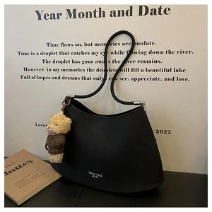 Detail of black crescent shoulder bag with silver logo and cute teddy bear charm