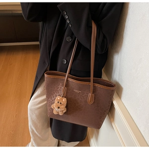 Close-up of brown leopard print tote bag with bear charm on a model in a black blazer