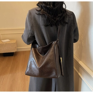 Detail view of a dark brown large tote bag in premium faux leather worn over a coat
