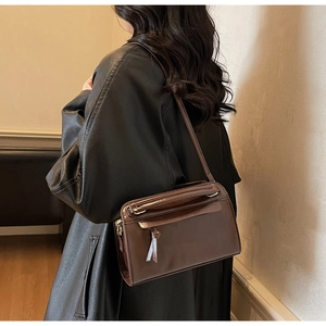 Détail d'un sac à bandoulière en cuir marron foncé avec pompon et fermeture éclair