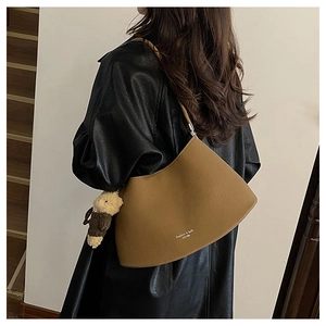 Close-up of brown leather shoulder bag with a cute plush bear charm on a model