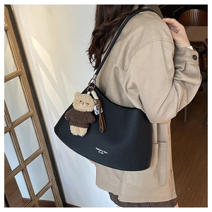 Detail of black leather hobo bag with teddy bear charm and fashion text worn by model