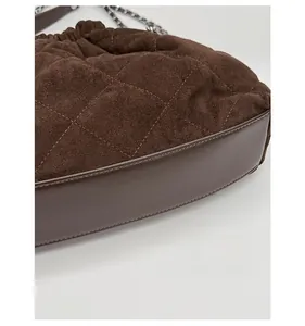 Detail of quilted brown suede bucket bag featuring silver metal logo and chain strap