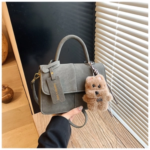 Close-up of grey suede handbag with round handle and cute plush dog charm accessory
