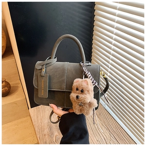 Detail of dark green retro square bag with white stitching and plush dog charm