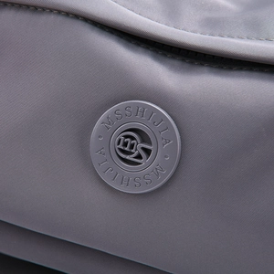 Detail shot of the circular rubber logo on water-resistant dark grey nylon shoulder bag