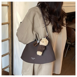 Detail of dark brown underarm bag with cute teddy bear charm on model in trench coat