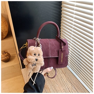Detail of burgundy textured tote with white stitching and plush dog charm accessory